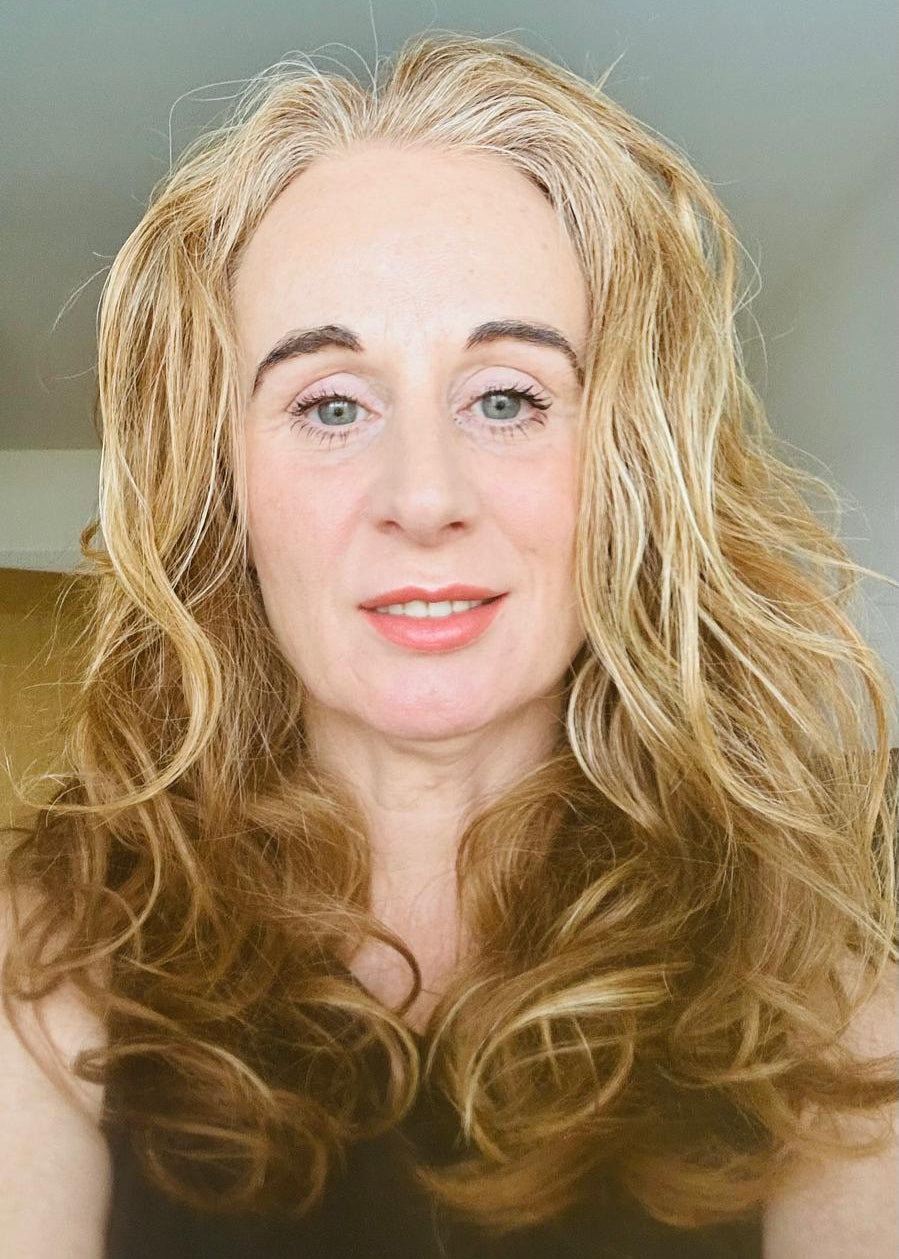 Woman with long blonde hair and a neutral expression against a plain background